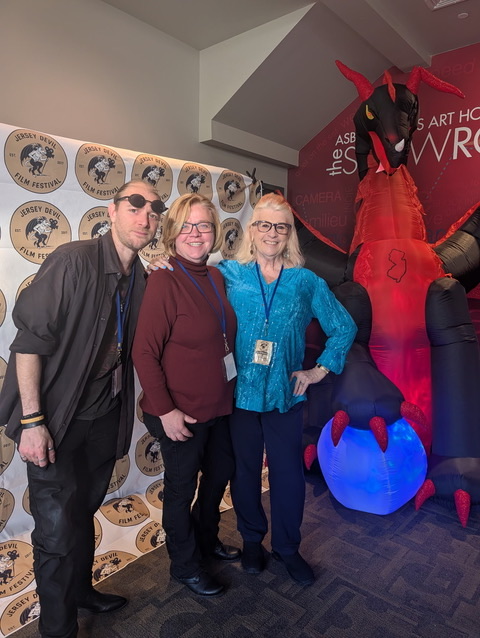Jersey Devil Film Festival organizers and attendees posing with a large Jersey Devil mascot and backdrop.